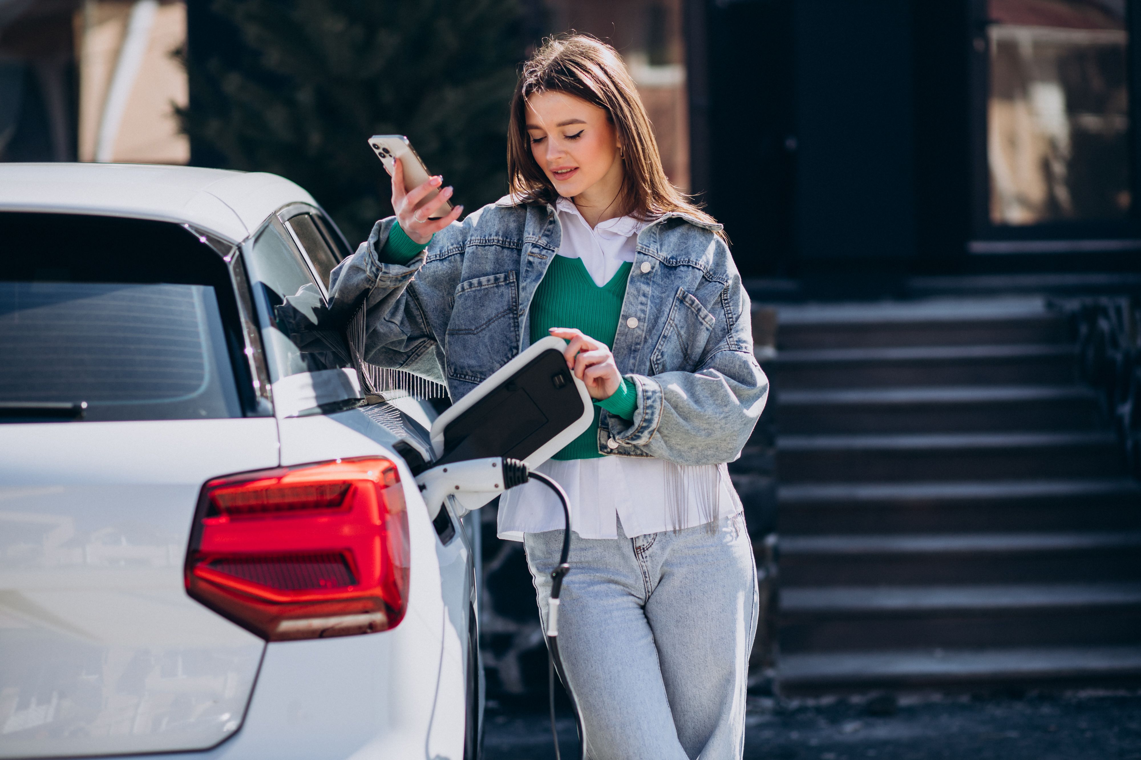 Mujer joven al lado de un coche eléctrico blanco que se está recargando